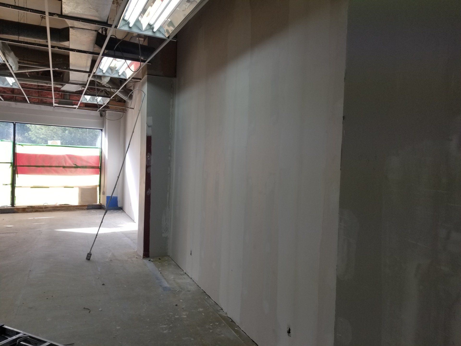 Intérieur d'un bâtiment inachevé avec plafond apparent, mur gris et ouverture lumineuse au fond.