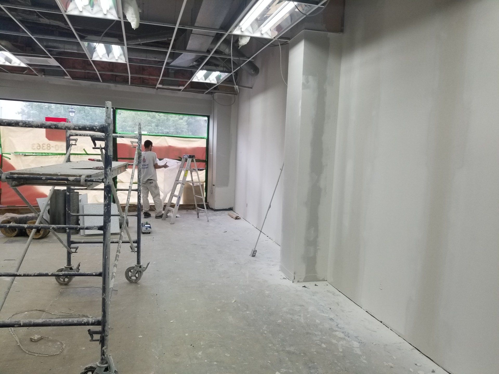 Intérieur d'un chantier de construction avec des ouvriers, des échafaudages et des murs blancs inachevés sous des poutres de plafond apparentes.