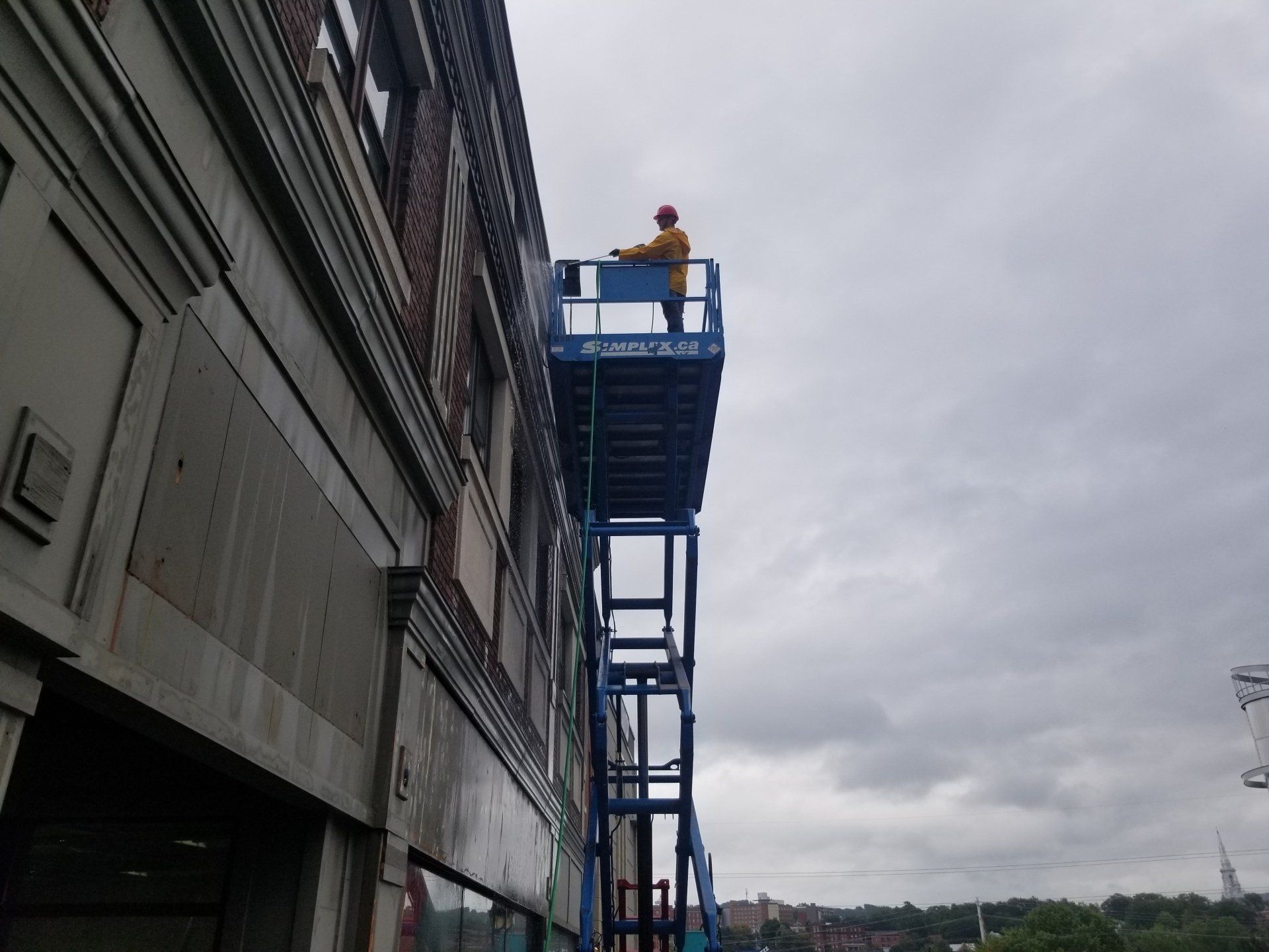 Ouvrier sur un ascenseur bleu à côté de la façade d'un immeuble sous un ciel nuageux