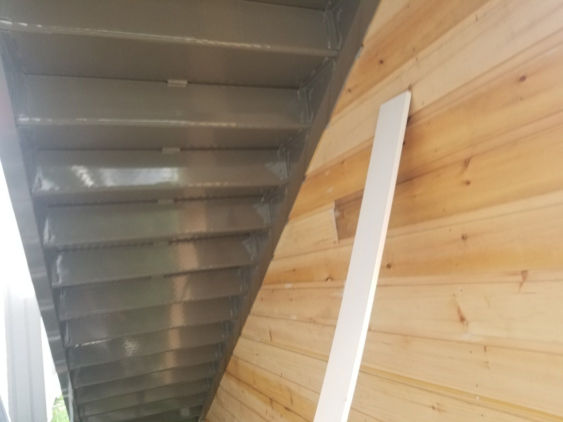 Vue intérieure d'un escalier en tôle ondulée jouxtant un mur lambrissé avec une plinthe blanche