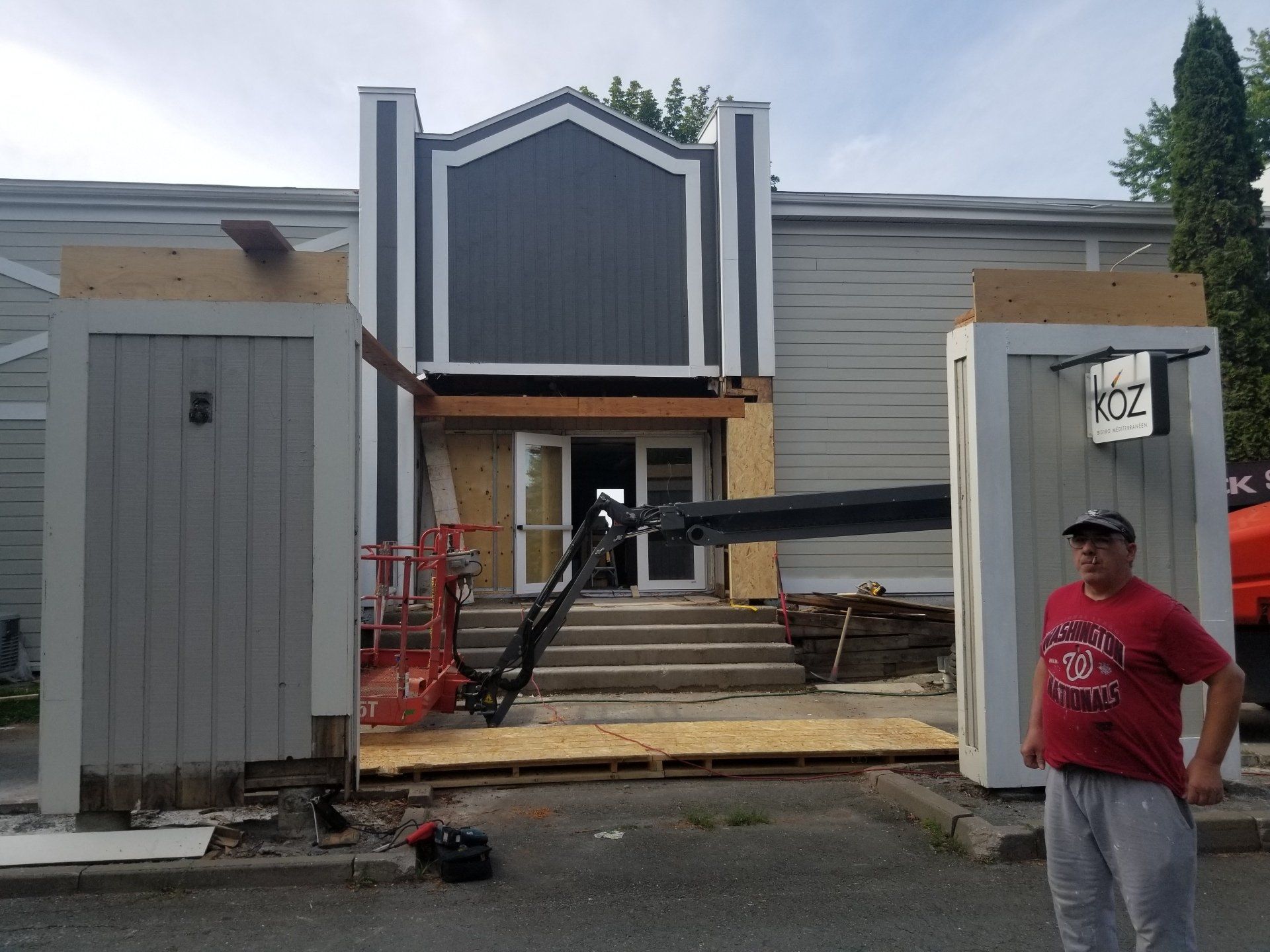 Chantier de construction avec façade en rénovation, échafaudages et un ouvrier debout près de l'entrée.