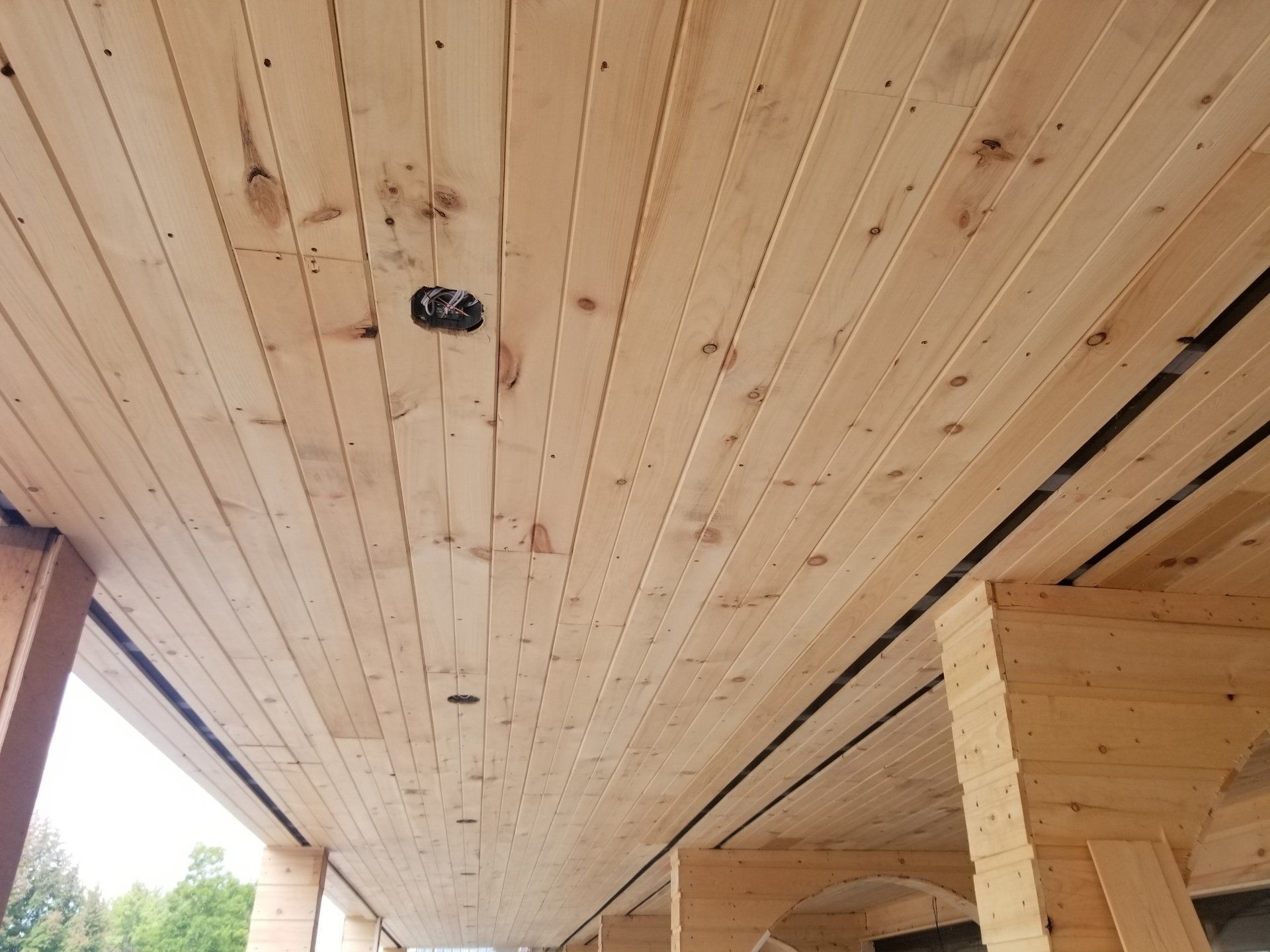 Plafond lambrissé en construction avec ouvertures pour éclairage encastré et poutres apparentes sur la droite.