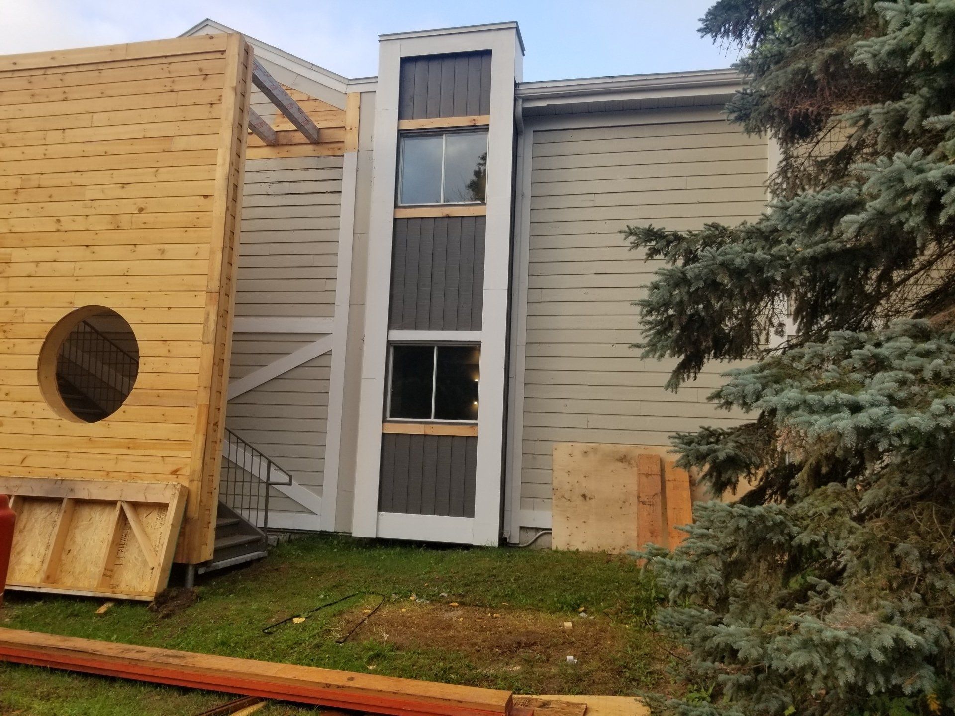 Extérieur de maison moderne avec un bardage beige, de hautes fenêtres étroites et un grand panneau mural en bois.