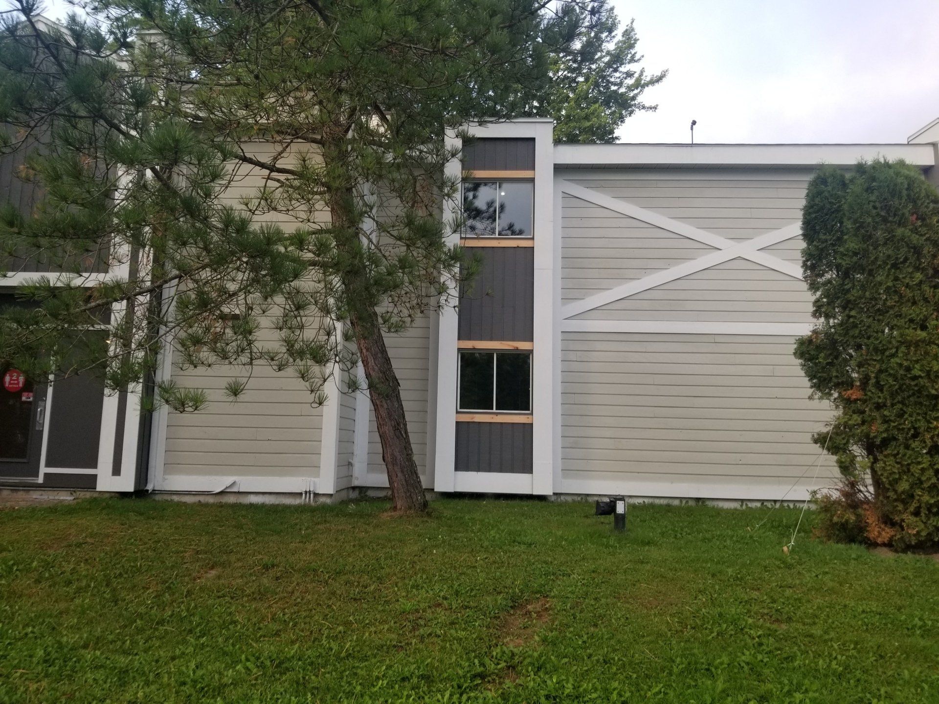 Extérieur d'une maison de banlieue avec un bardage beige, un arbre devant et une pelouse verte.