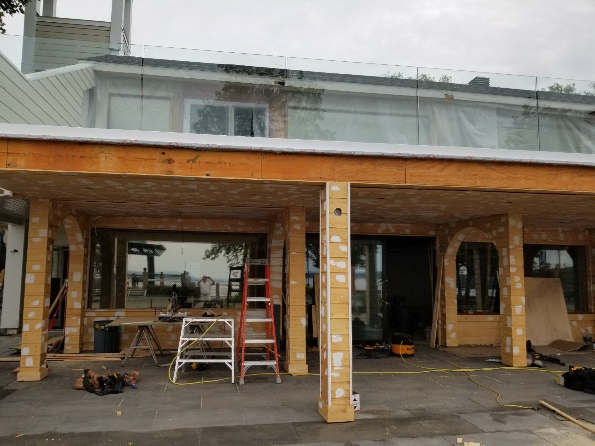 Extérieur de la maison en construction avec des poteaux en bois, une échelle et des outils sur la terrasse couverte