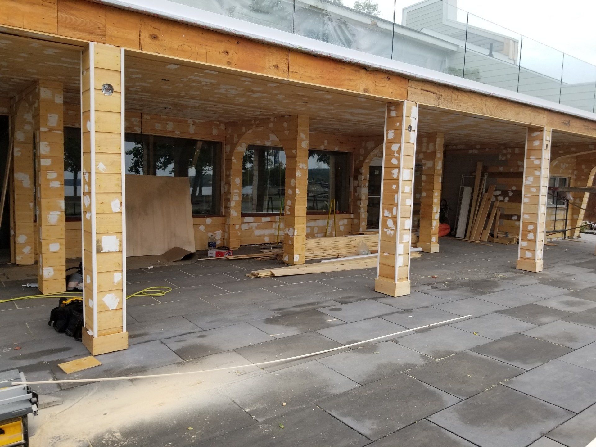 Allée extérieure couverte avec poteaux en bois, portes vitrées et matériaux de construction au sol