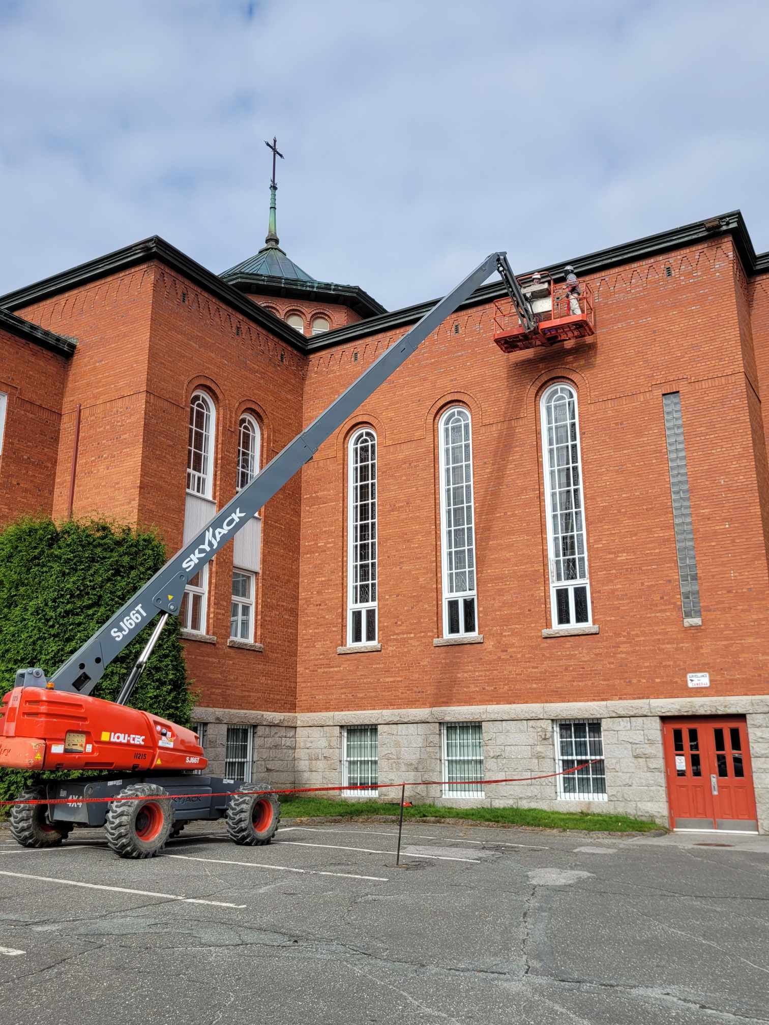 Une nacelle élévatrice se déploie pour inspecter un bâtiment d'église en briques avec de hautes fenêtres cintrées.
