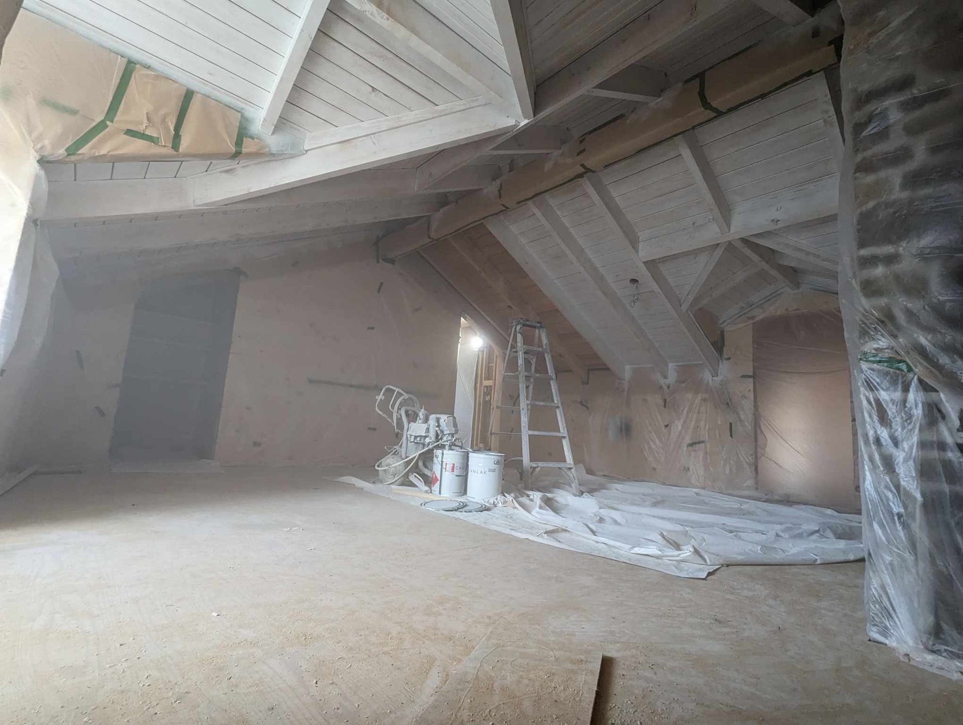 Grenier non aménagé avec poutres apparentes, isolation et matériaux de construction sous un toit en pente.