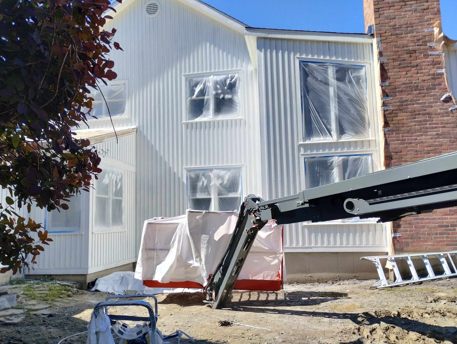 Extérieur d'une maison blanche avec des engins de chantier et une échelle dans la cour sous un ciel bleu clair