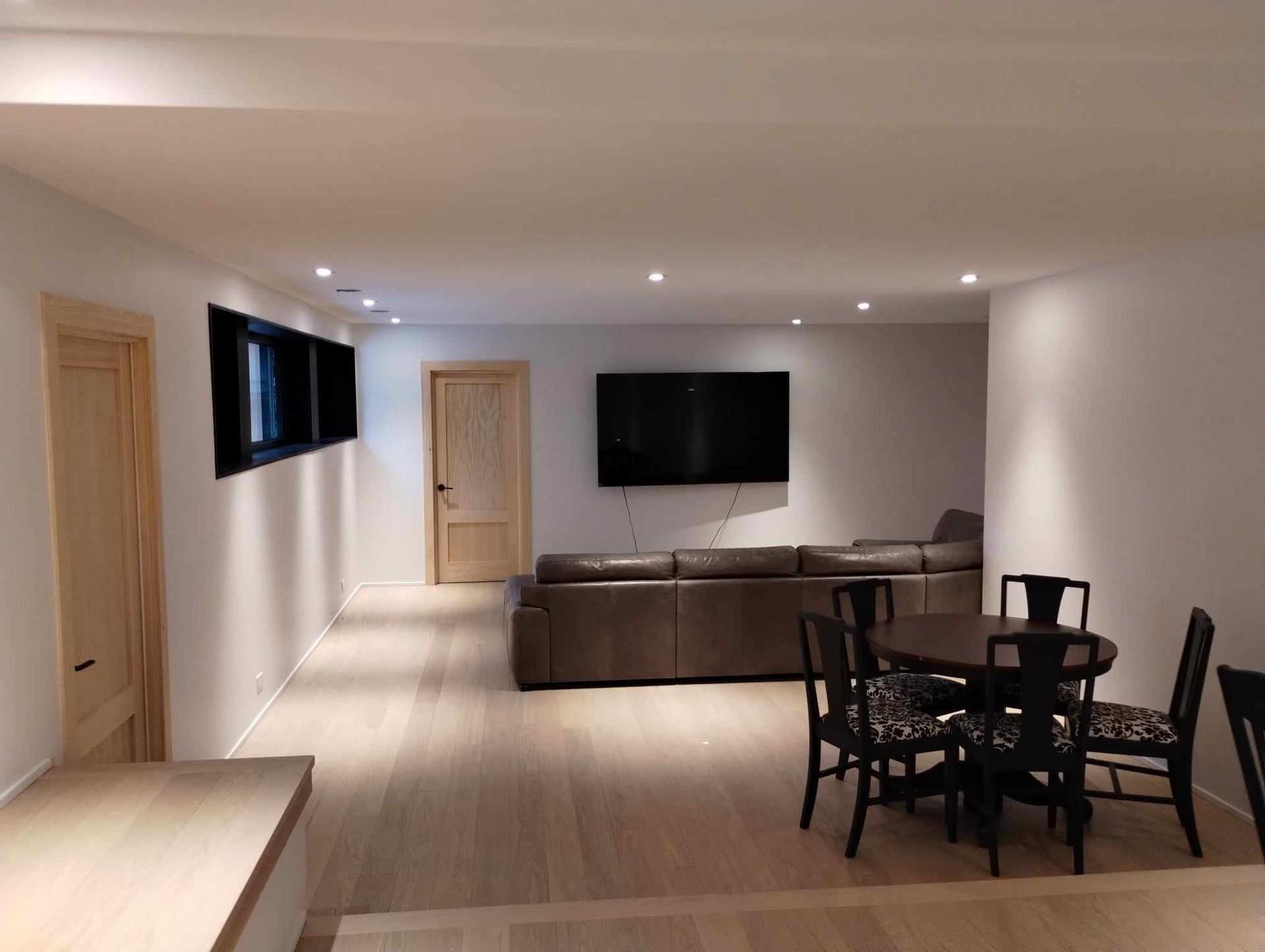 Salon moderne à aire ouverte avec canapé d'angle marron, table à manger, télévision murale et parquet clair