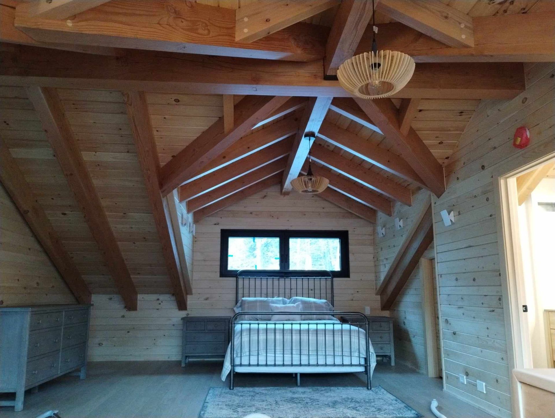 Chambre mansardée avec poutres apparentes, un lit et une petite fenêtre au fond.
