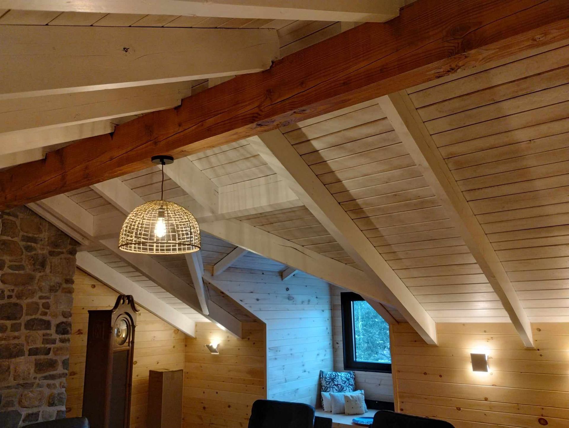 Chambre mansardée rustique avec poutres apparentes, mur en pierre, lanterne suspendue et coin fenêtre éclairé en bleu