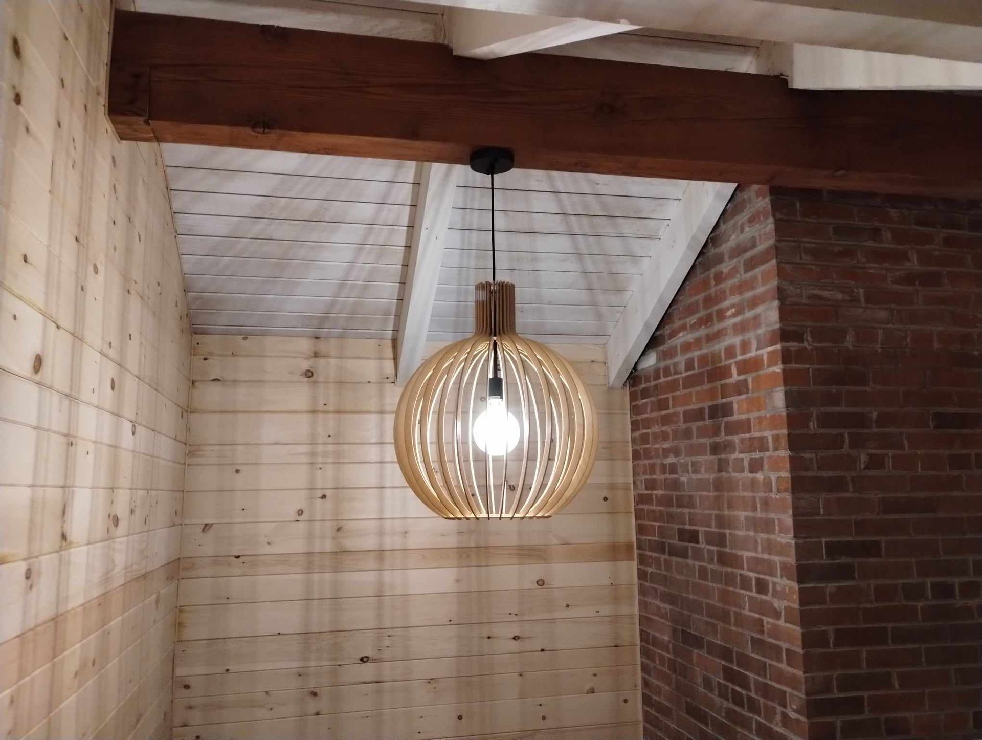 Suspension en bois avec ampoule apparente, suspendue au plafond d'une pièce rustique aux murs de briques et lambris.