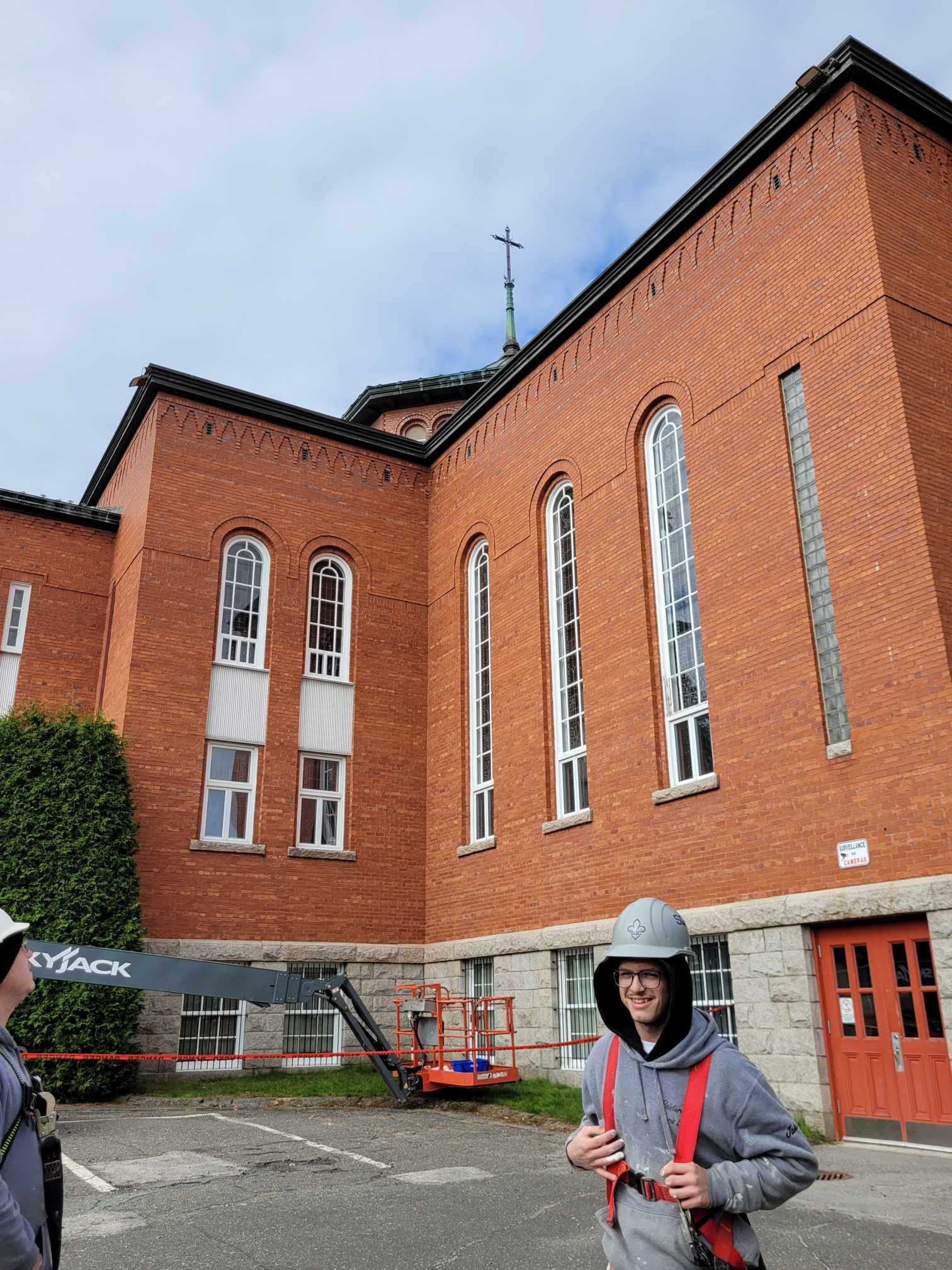 Cour intérieure d'un bâtiment en briques rouges, avec une personne portant un sweat à capuche gris et un sac à dos rouge se tenant devant.