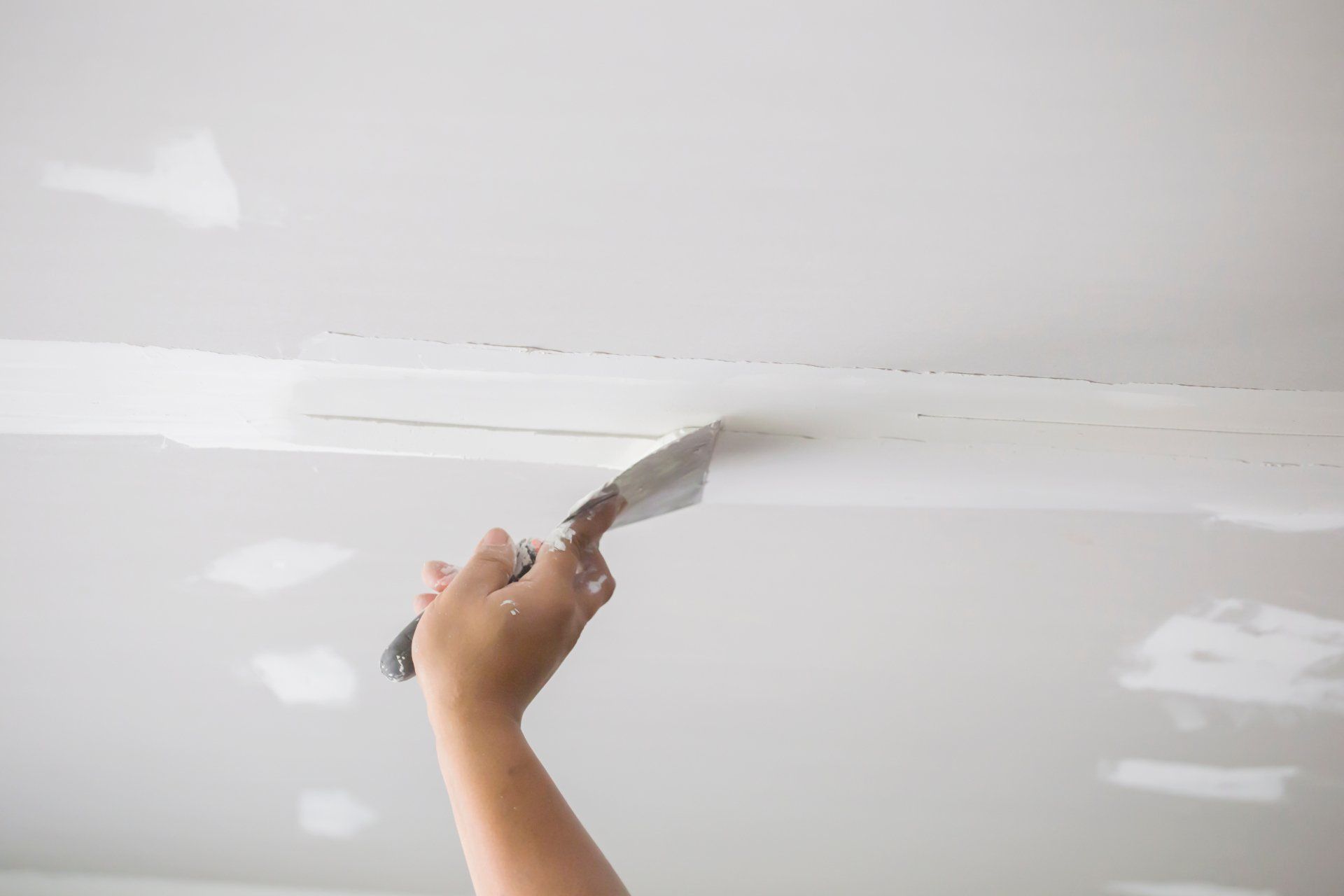 Application manuelle d'enduit à joints de plaques de plâtre sur un joint de plafond à l'aide d'un couteau à mastic