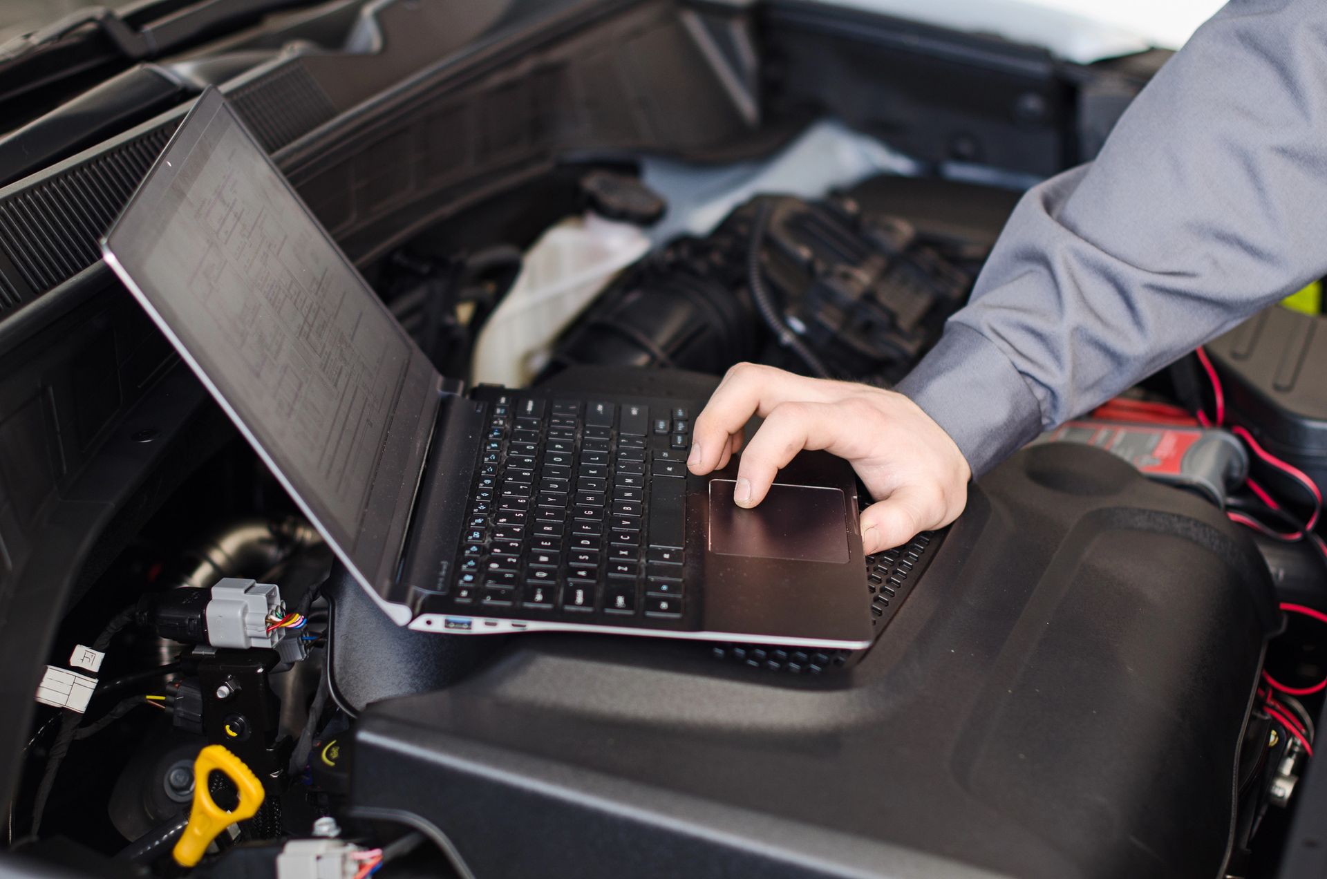 Un meccanico utilizza un computer portatile per diagnosticare un problema al motore di un veicolo, situato sotto il cofano.