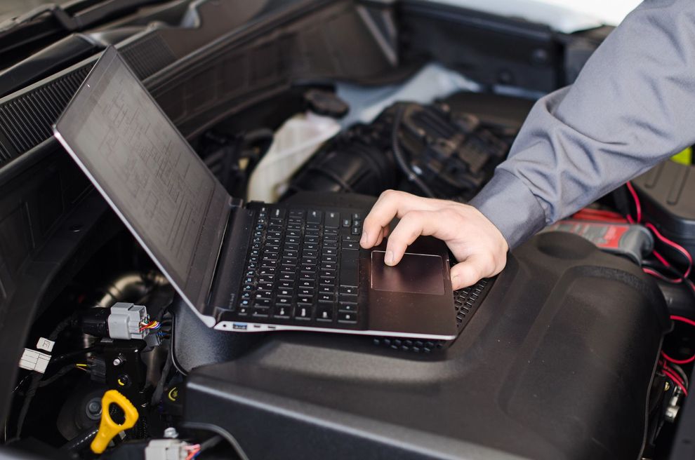 Un meccanico utilizza un computer portatile per diagnosticare un problema al motore di un veicolo, situato sotto il cofano.
