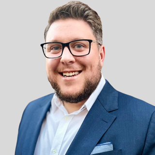 Man with glasses smiles broadly in a blue suit.