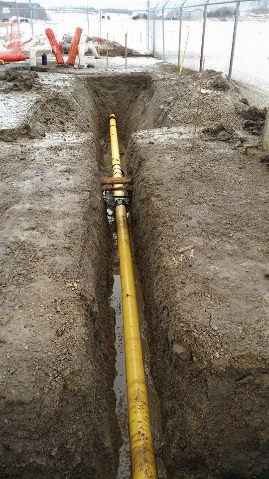 A long yellow pipe runs through the center of a muddy construction trench outdoors, viewed from above.