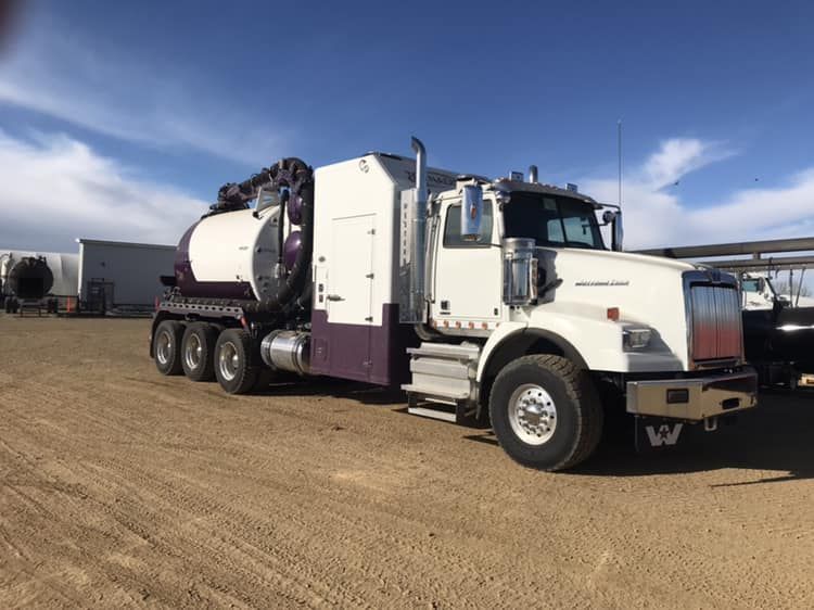 A white Western Star vacuum truck parked on a gravel lot under a blue sky.