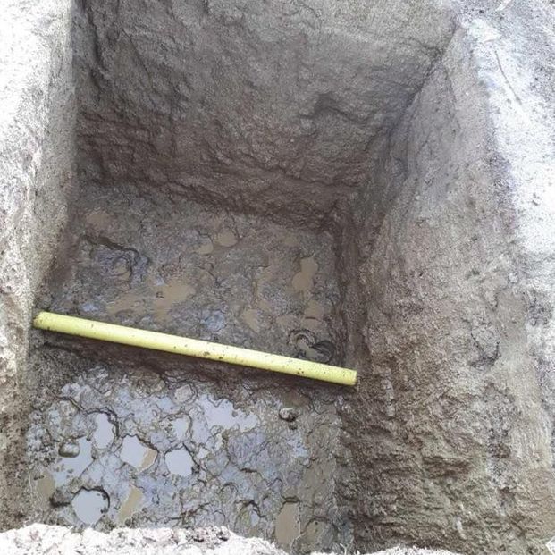 A yellow pipe crosses the center of a deep, square-shaped excavation in muddy, water-filled soil.