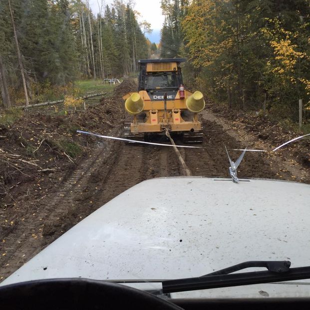 A view from a vehicle hood showing a yellow bulldozer towing it through a muddy, forest trail.