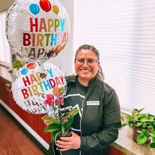 Woman smiling with birthday balloons and a potted orchid in a hallway