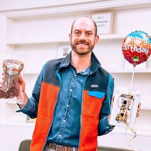 Smiling man holding birthday balloons and wrapped gifts indoors