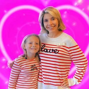 Two people in red-and-white striped shirts smiling against a bright pink heart background