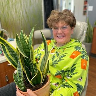 Smiling person in neon green shirt holding a potted snake plant indoors