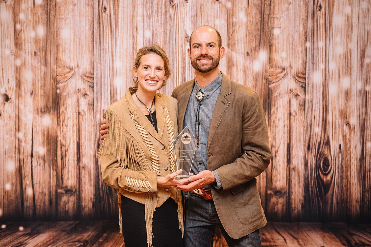 Two people holding a trophy in front of a rustic wooden backdrop