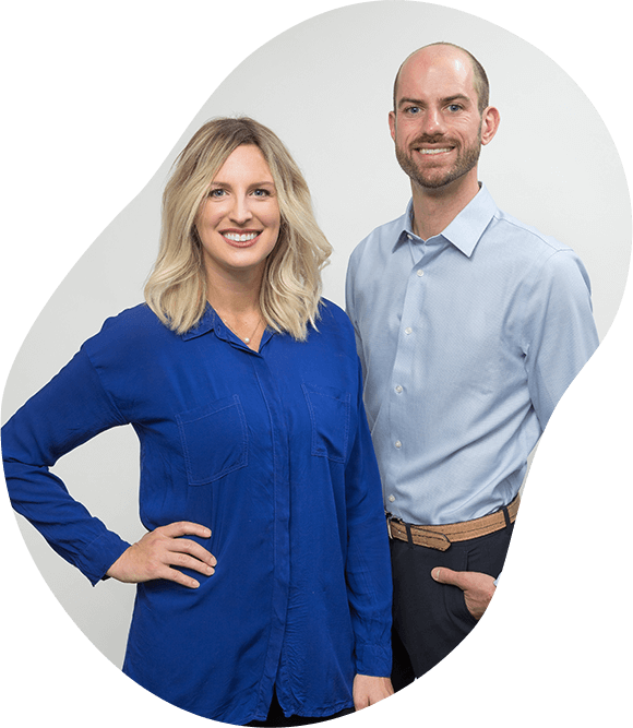 Two business professionals posing against a light gray background, smiling