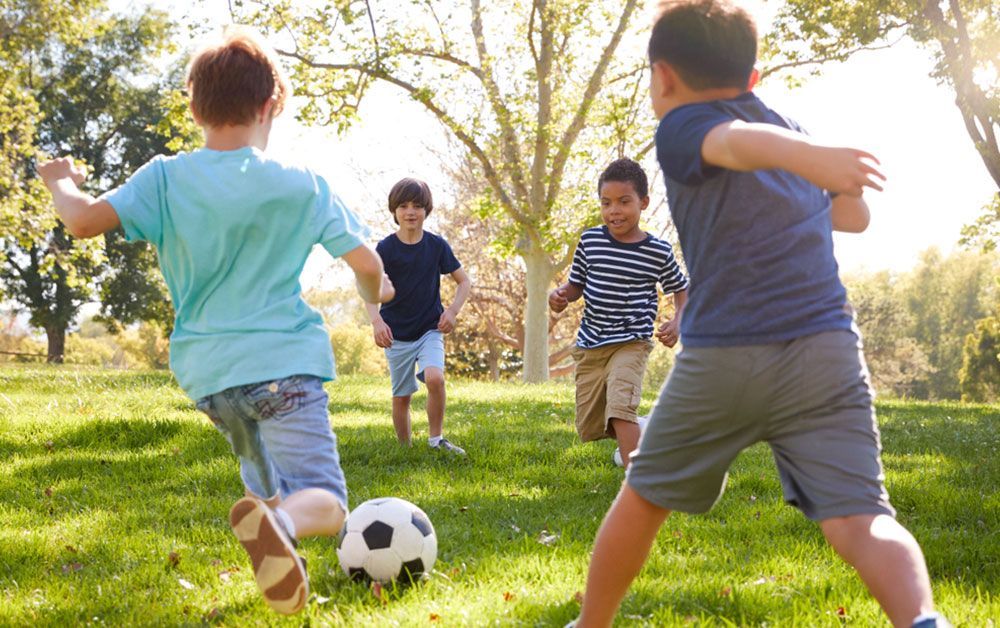Children playing soccer in a sunny park, with one child kicking the ball and others running nearby.