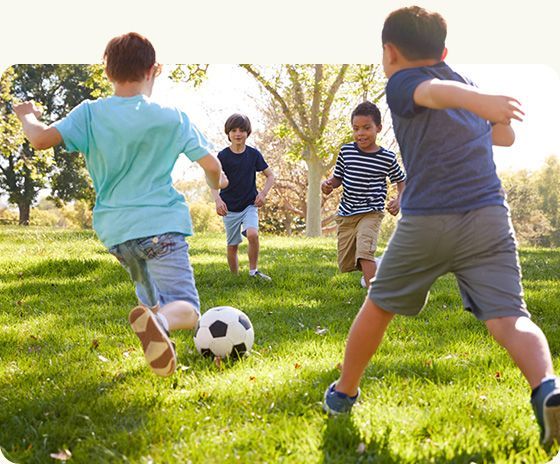 Children playing soccer on a sunny grassy field with a ball in the foreground