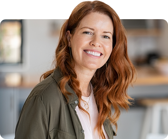 Smiling woman with red hair in a casual green jacket, seated indoors with a blurred office background