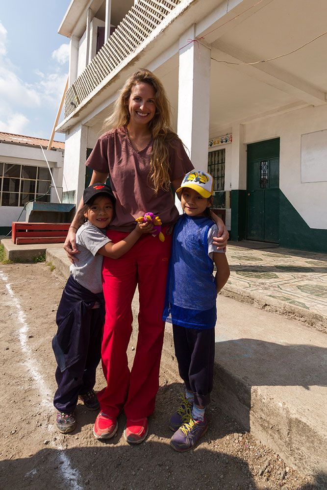 Woman standing with two children outside a building, all smiling, one child in a yellow cap.