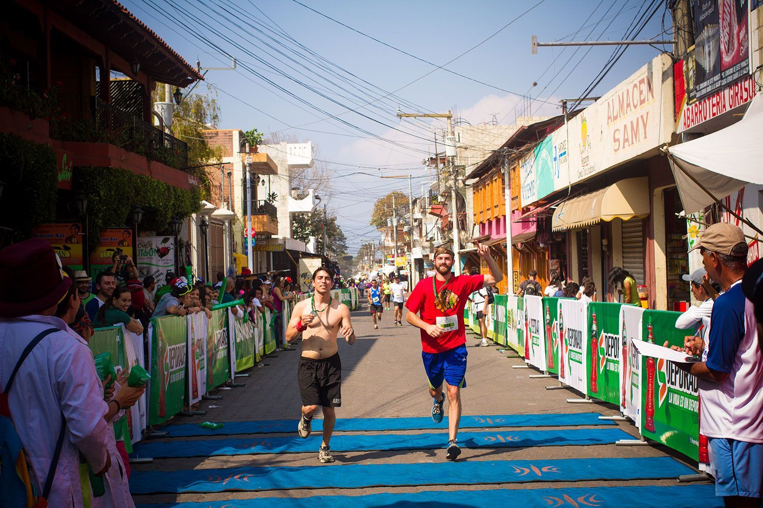 Two runners race down a blue-marked street lined with colorful spectators and banners.