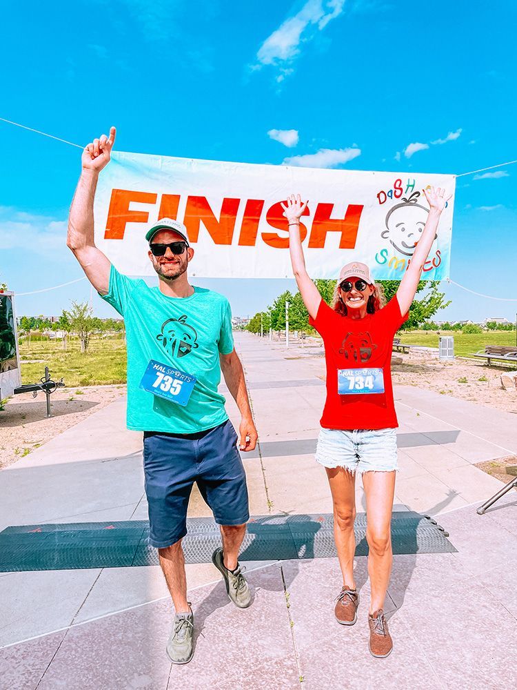 Two runners crossing the finish line with arms raised on a sunny outdoor path