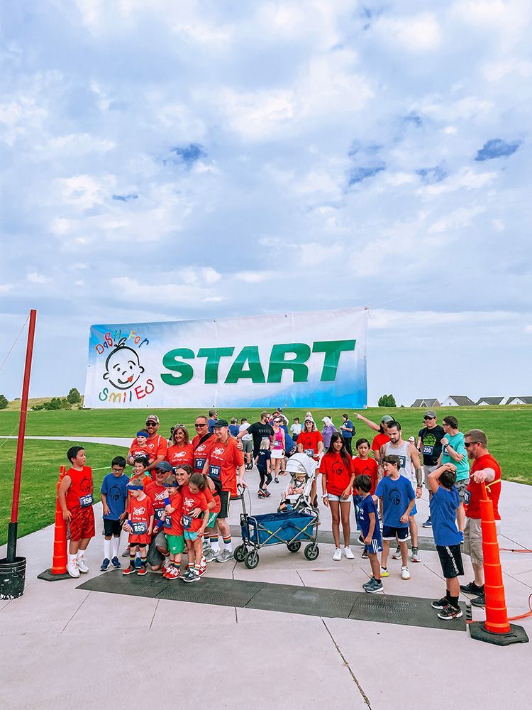Group of people at a race start line under a green “START” banner, outdoors on a cloudy day