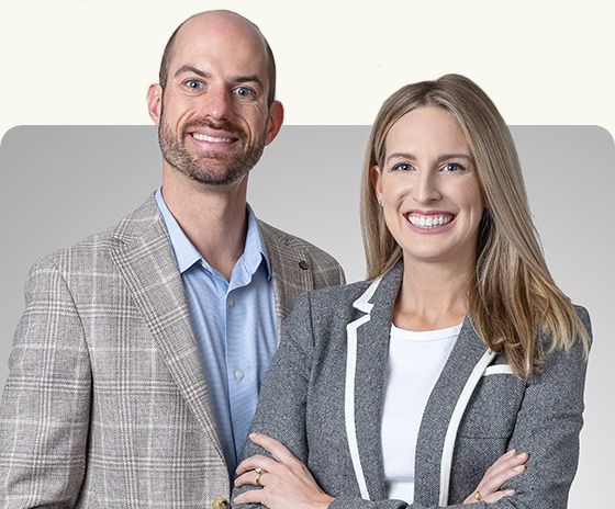Two smiling professionals in business attire standing together against a light gray background
