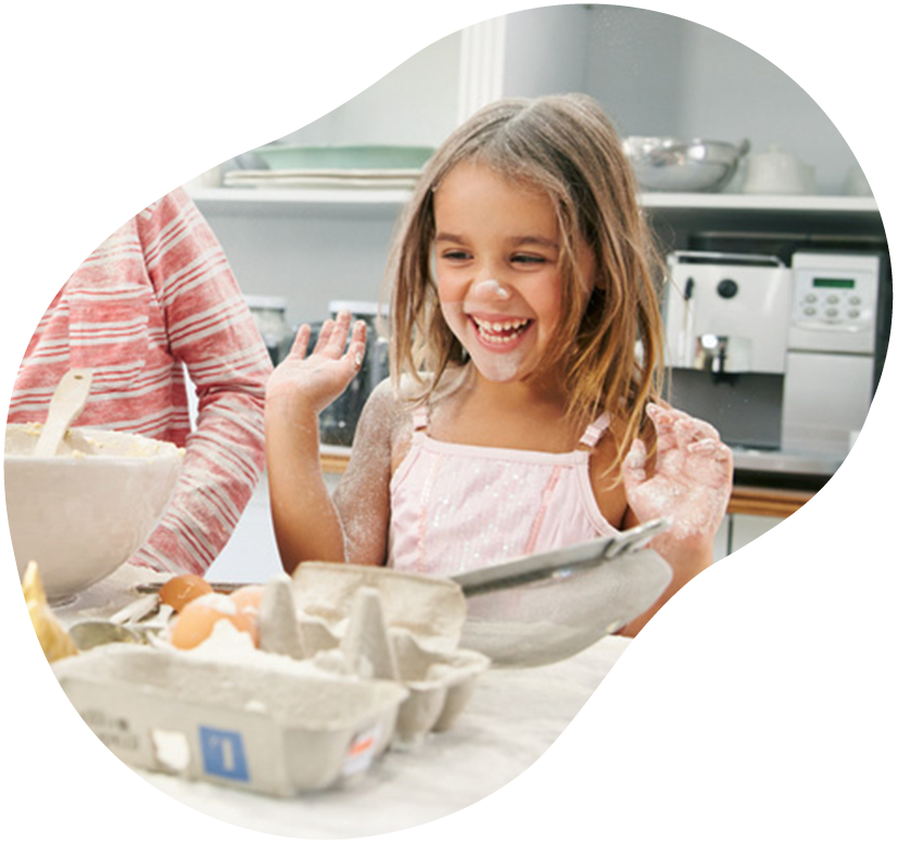 Child smiling and holding up a cracked egg while baking in a kitchen