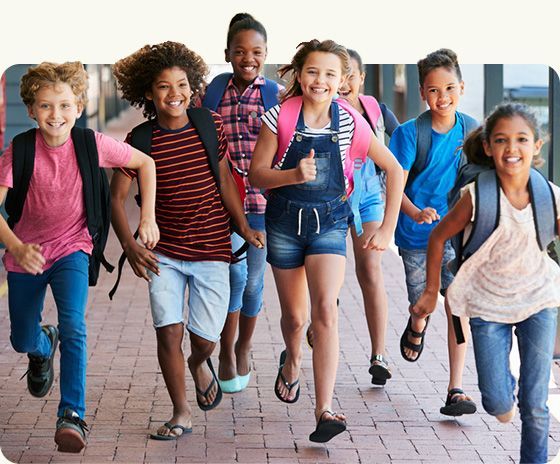 Children walking and smiling with backpacks on a school sidewalk