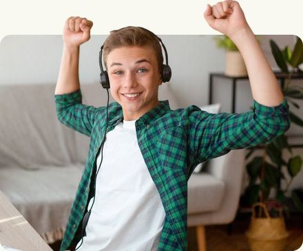 Smiling person in a green plaid shirt and headphones, raising both arms in a bright living room.
