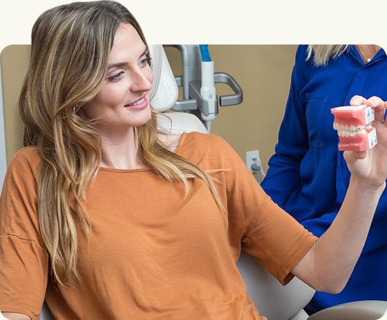 Woman in an orange shirt smiling while holding a dental teeth model in a clinic.