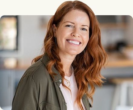 Smiling red-haired woman in an olive jacket indoors with a blurred office background