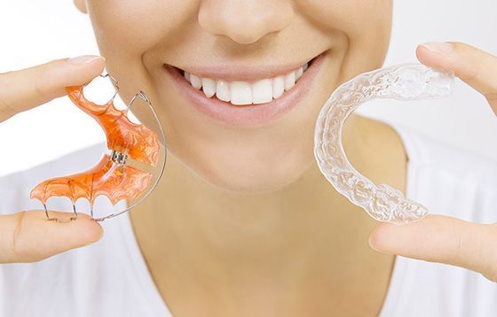 Smile wearing clear aligners while holding orange and transparent dental trays