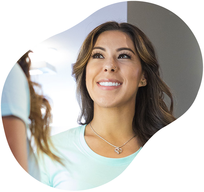 Smiling woman looking into a mirror, wearing a light blue top and necklace