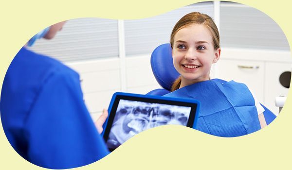 Dentist showing X-ray on tablet to smiling patient in blue dental bib