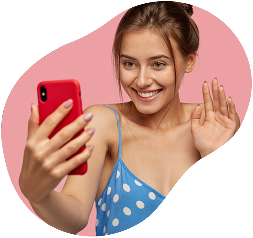Woman in blue polka-dot top taking a selfie and waving, smiling at the camera on a pink background