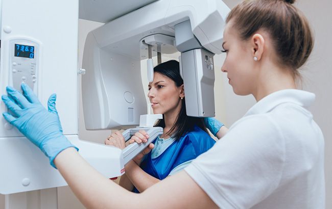 Technician adjusts mammogram machine while patient stands in a clinic